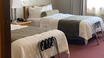 Una habitación de hotel con dos camas, una mesita de noche con lámpara y teléfono, un cuadro en la pared y una ventana con cortinas.