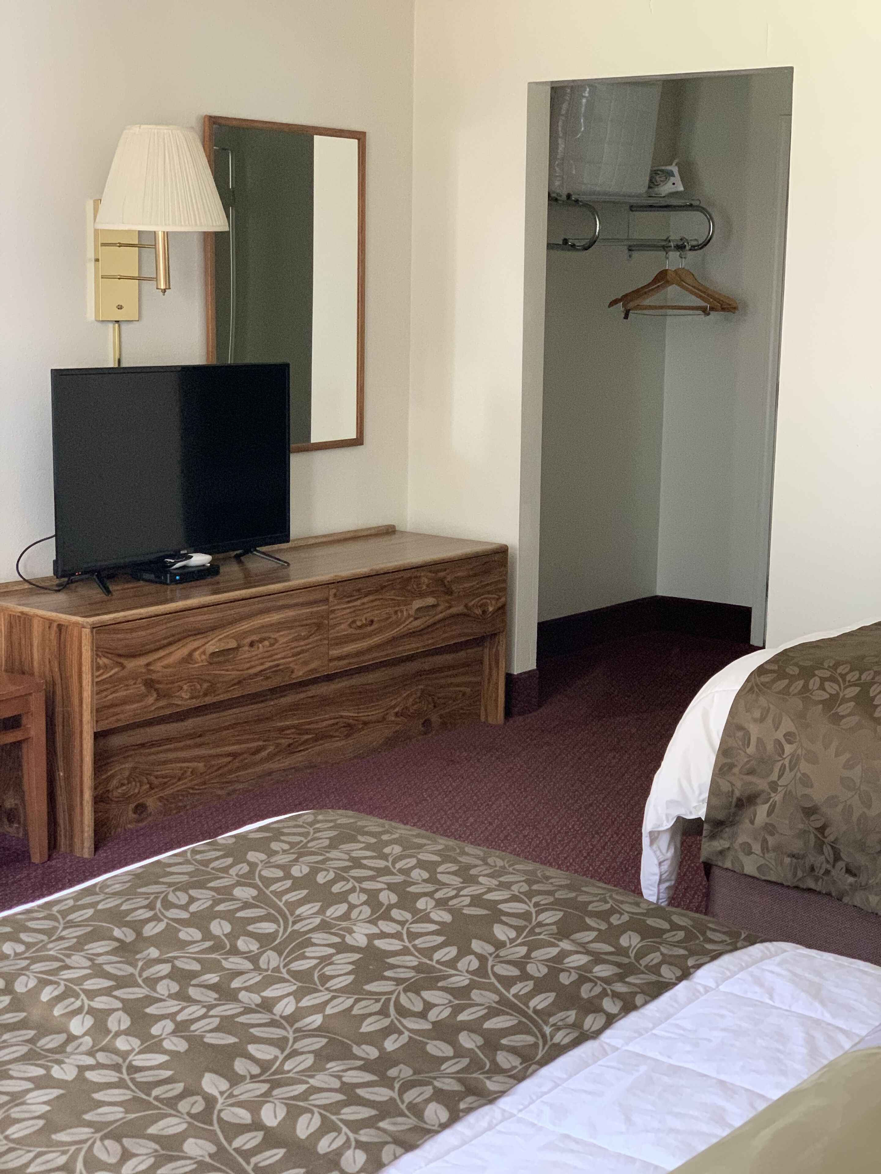 A hotel room with a bed, a wooden dresser, a television, a mirror, and a coat rack.