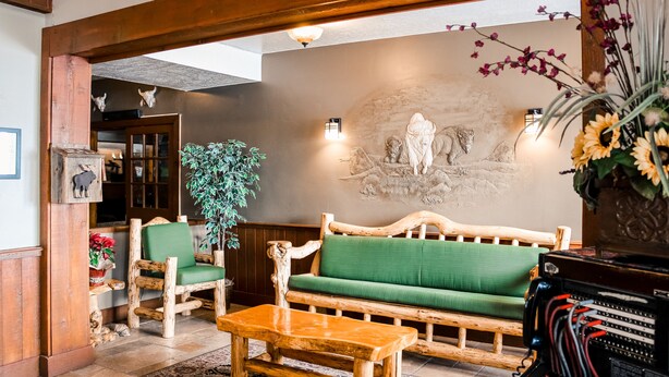 A wooden bench, a wooden sofa, and a wooden table in a room with a stone wall and a wooden ceiling. - White Buffalo (West Yellowstone)