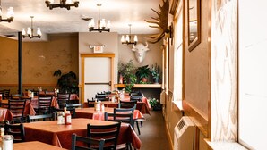 A restaurant interior with multiple tables and chairs, a mounted deer head on the wall, and a sign indicating an exit. - White Buffalo (West Yellowstone)