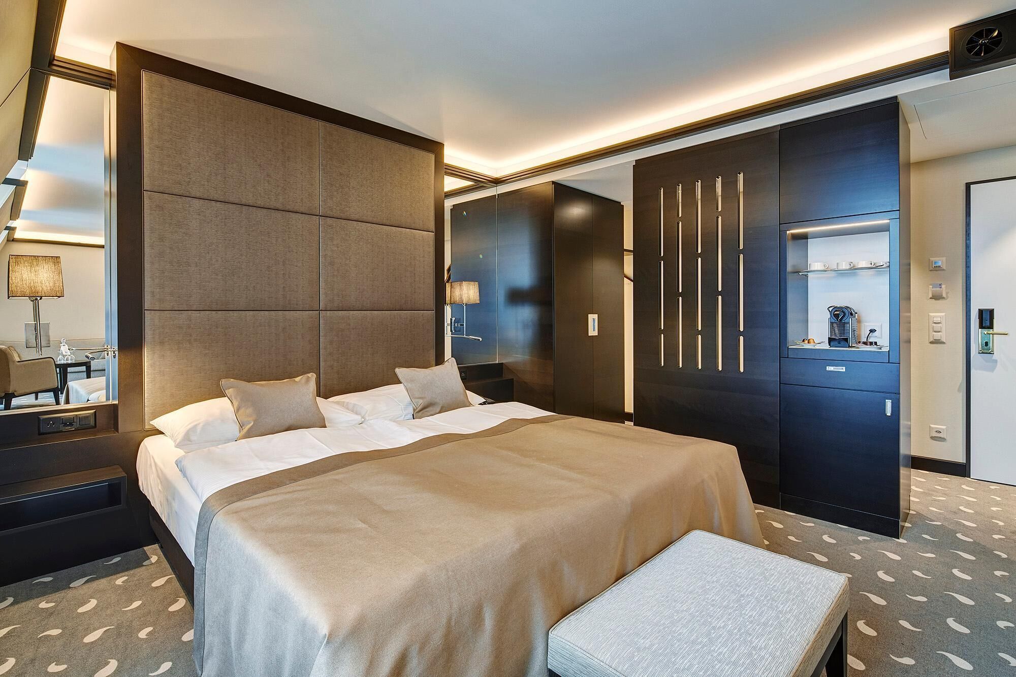A modern hotel room with a large bed, bedside tables, a desk, and a wardrobe.