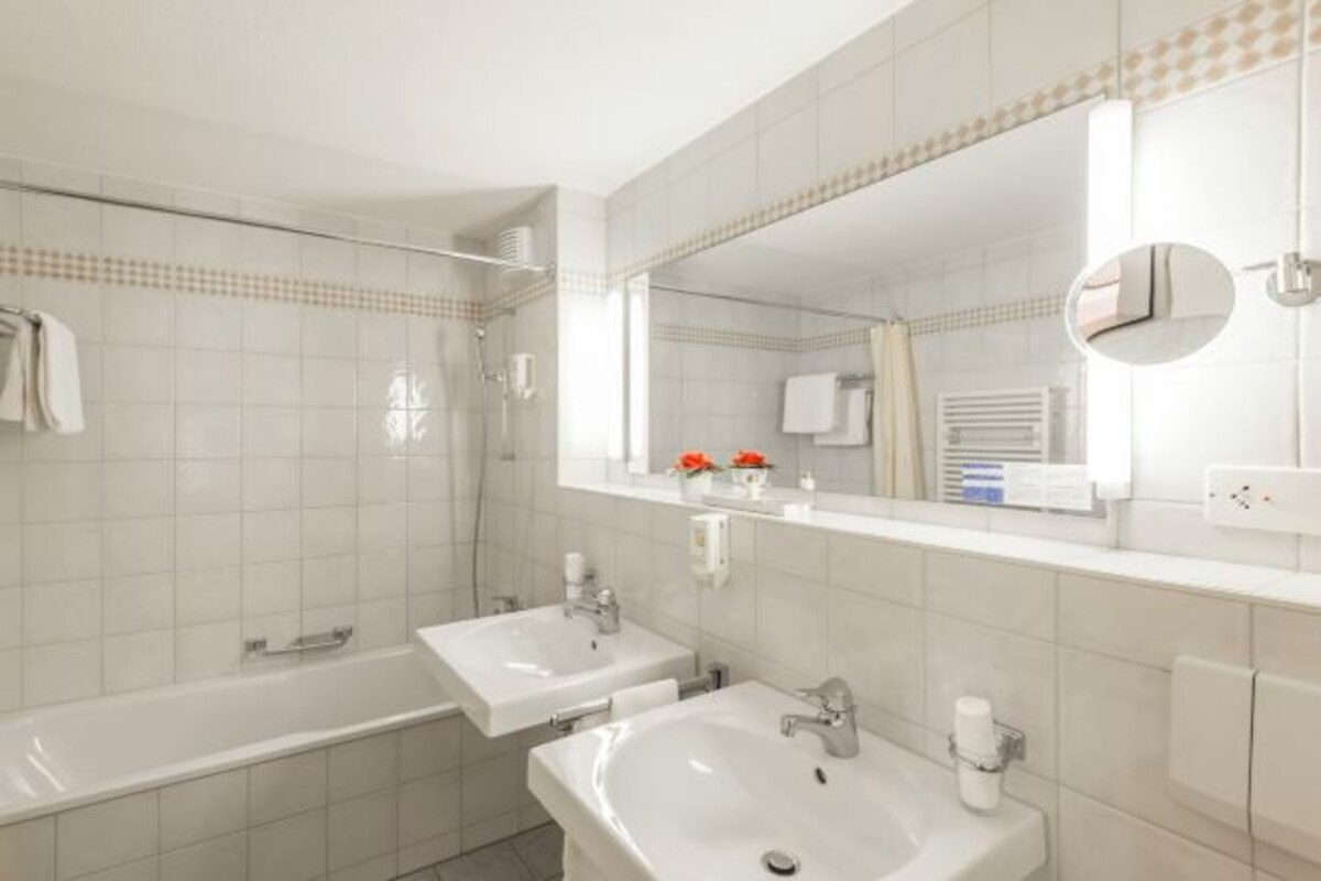 A modern bathroom with two sinks, a bathtub, and a large mirror.