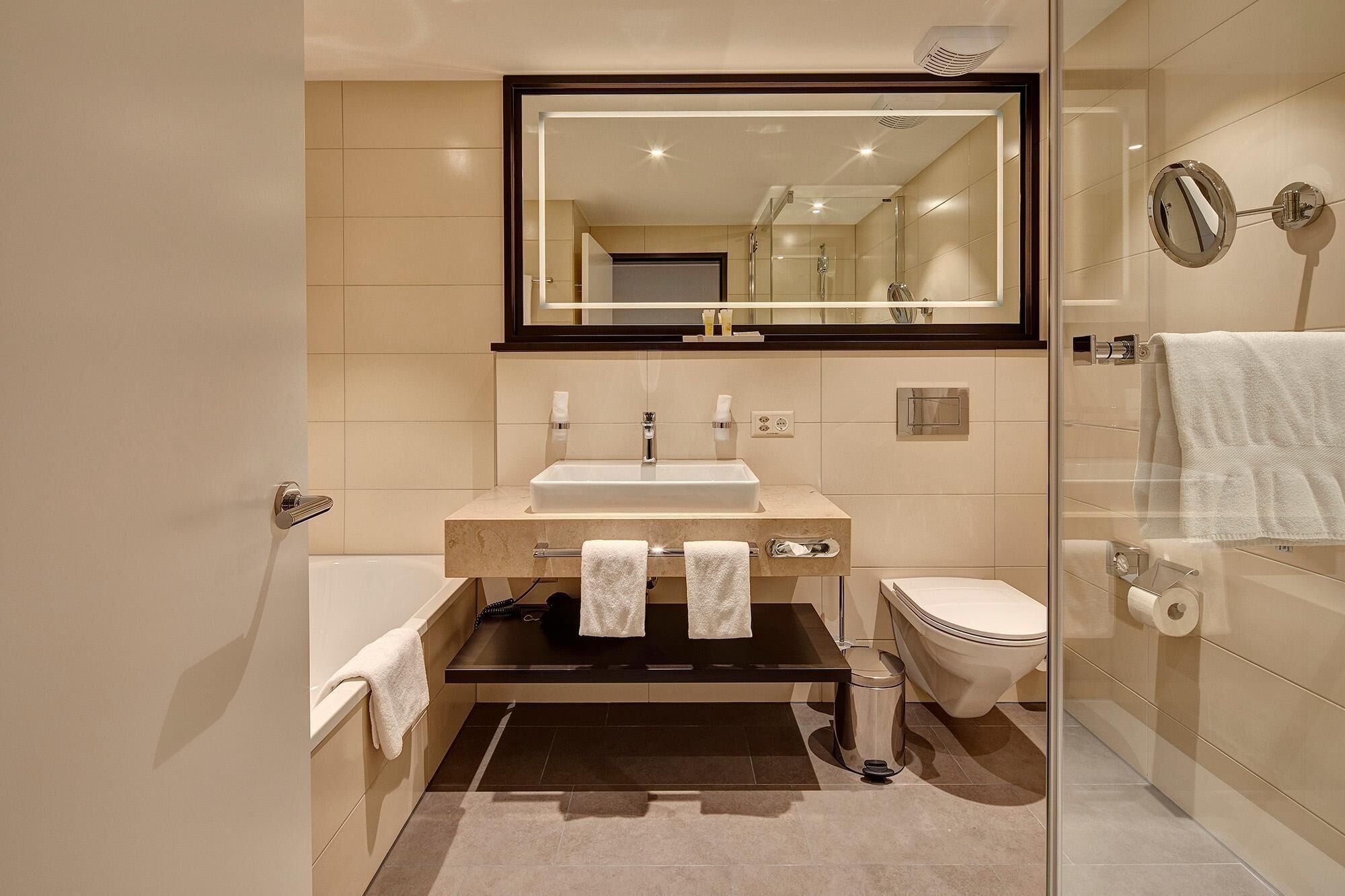 A modern bathroom with a large mirror, a sink, a toilet, and a shower area.