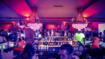 Un bar concurrido con una barra central y dos grandes candelabros.