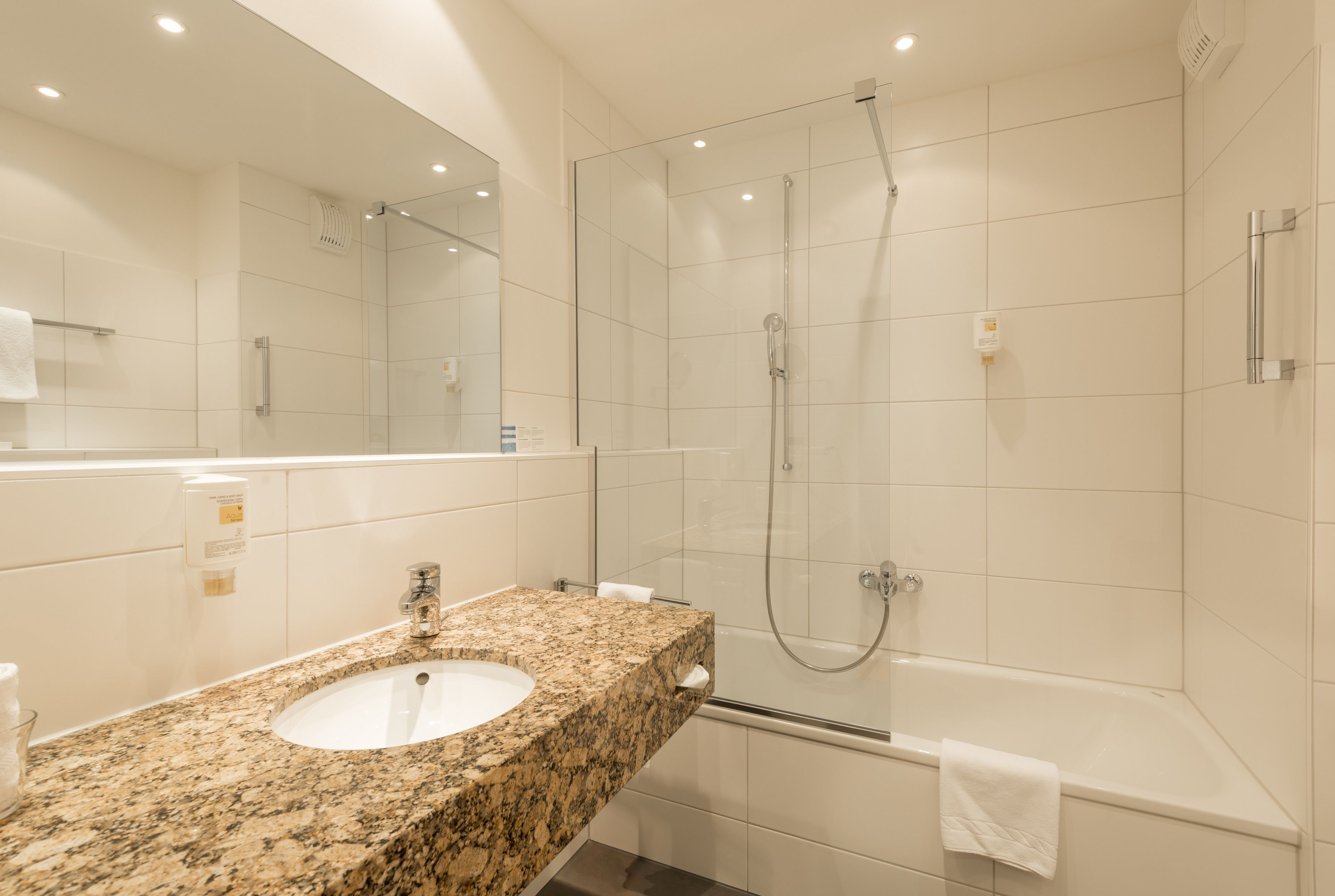 Un baño moderno con lavamanos de granito, ducha con cerramiento de vidrio y bañera independiente.