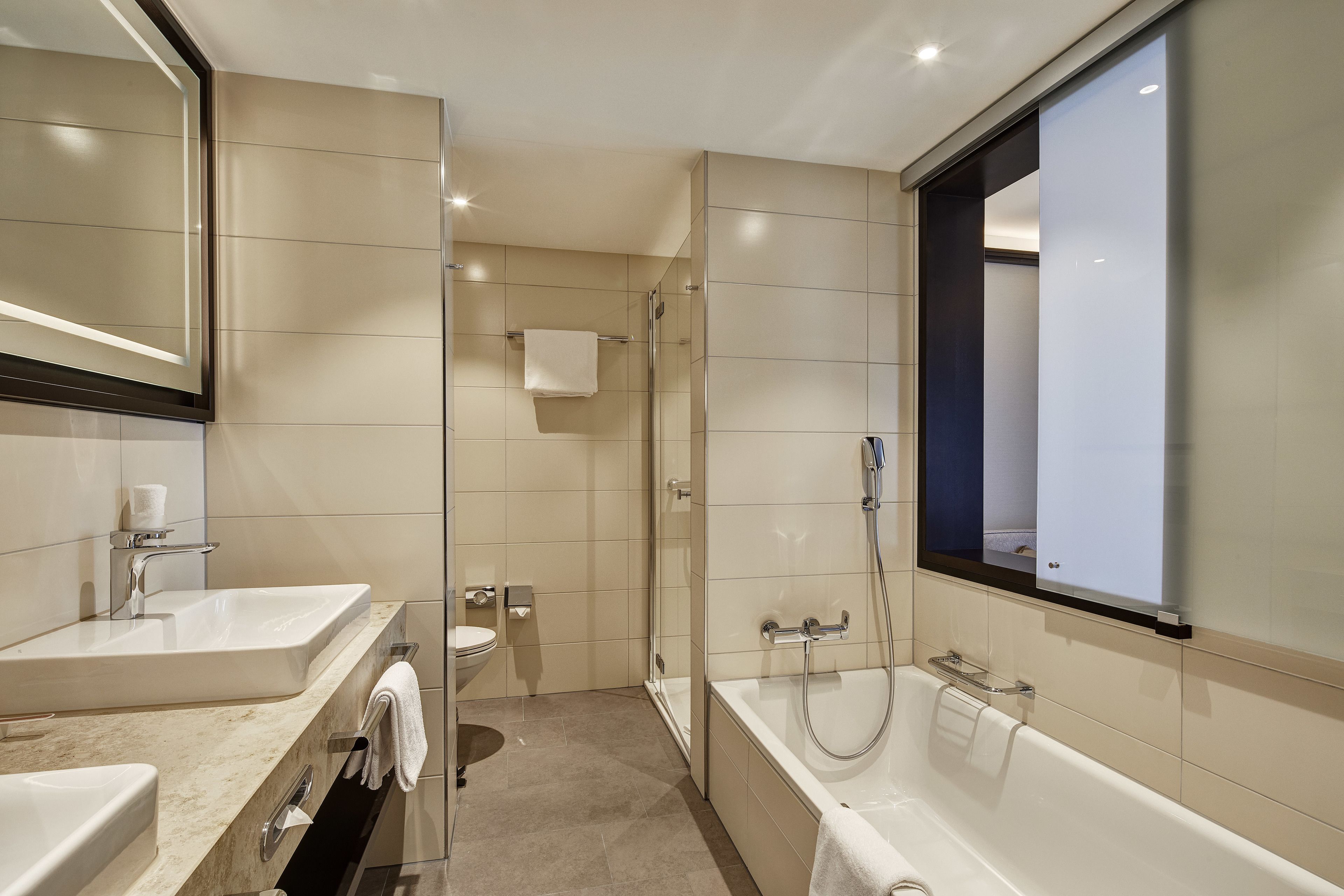 Une salle de bain moderne avec un grand miroir, deux lavabos, une baignoire et une douche.