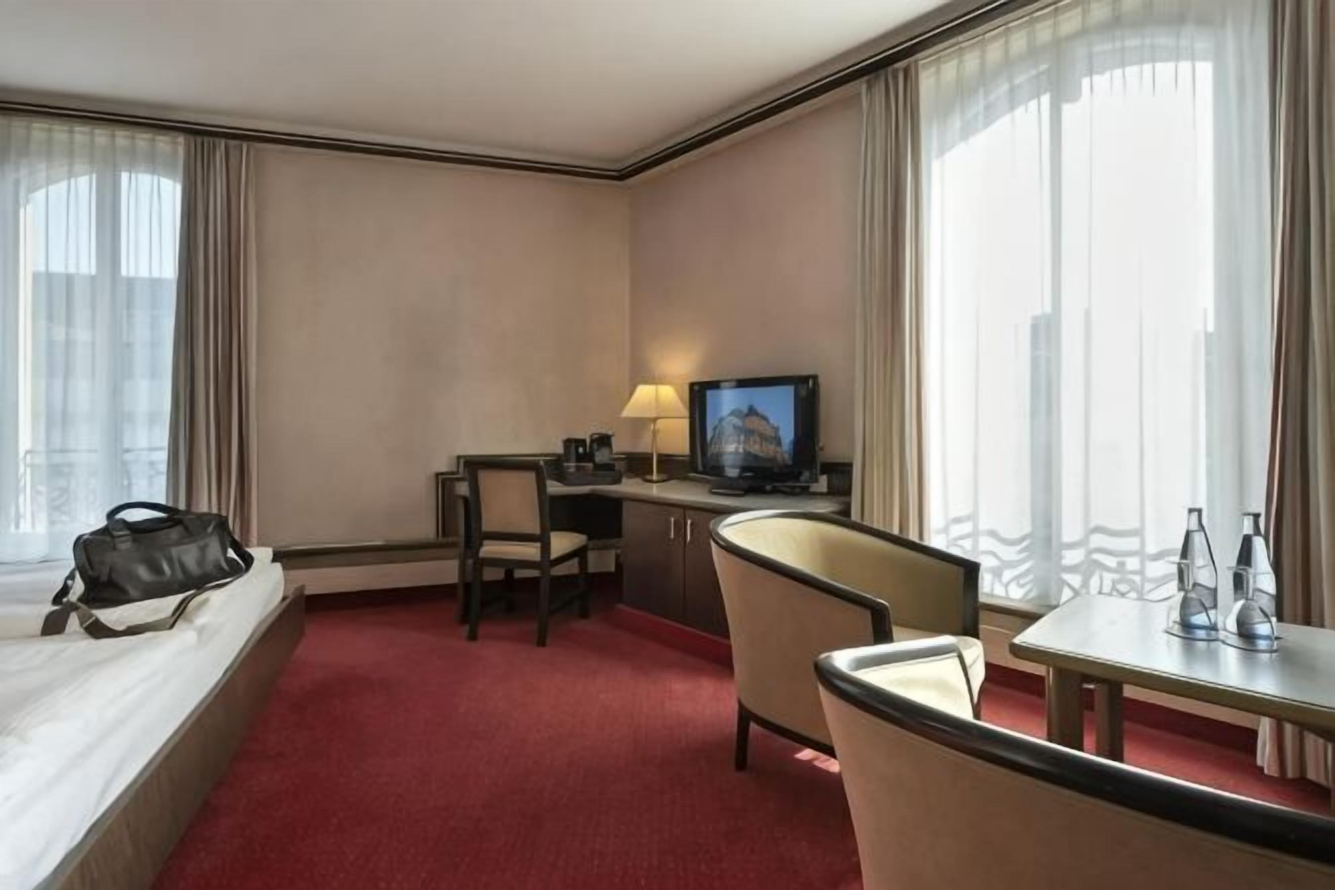 Une chambre d’hôtel équipée d’un lit, d’un bureau, d’une chaise, d’une télévision et de grandes fenêtres.