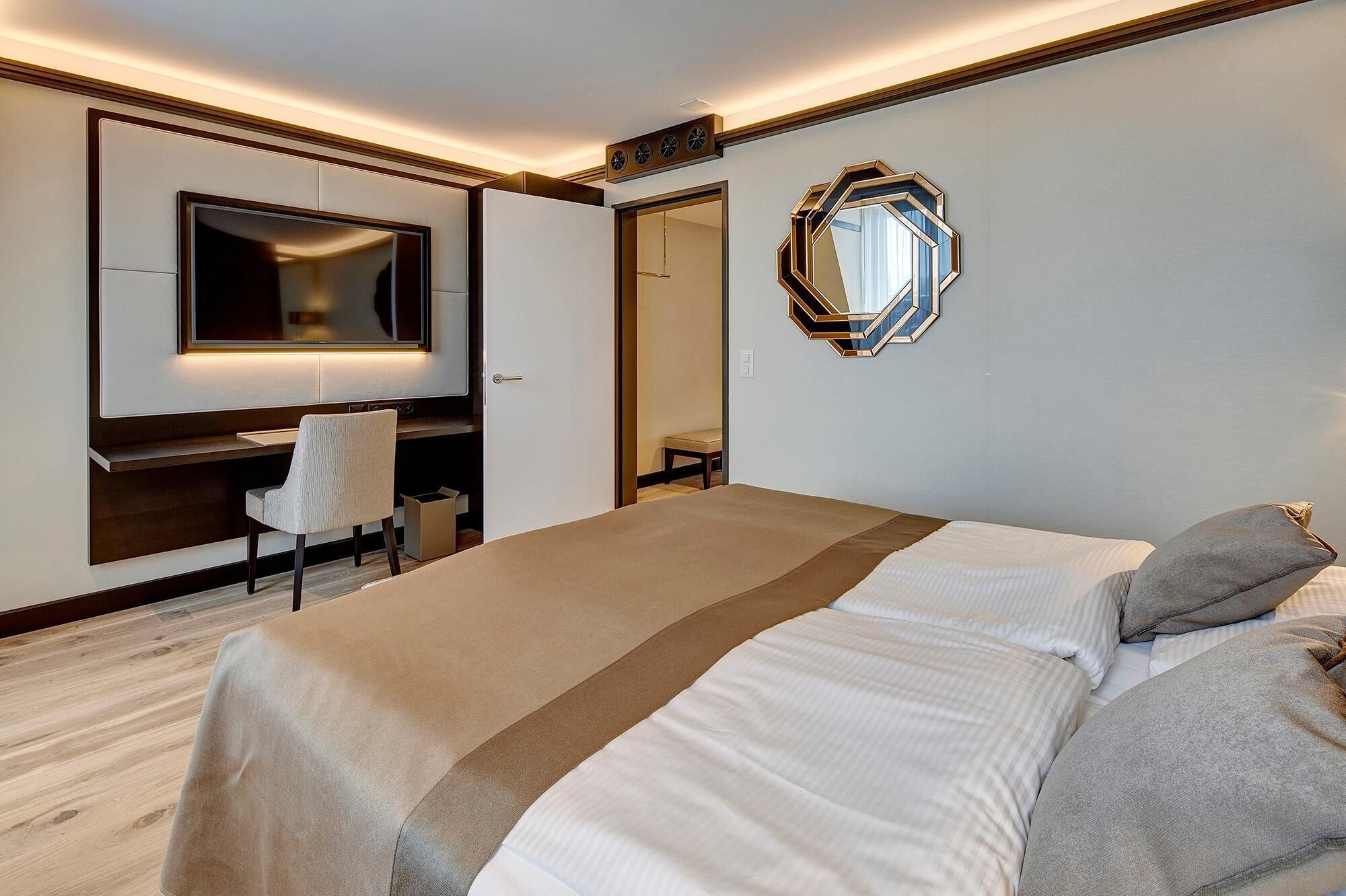 Ein Hotelzimmer mit Bett, Schreibtisch, Stuhl, Spiegel und einer Wanduhr.