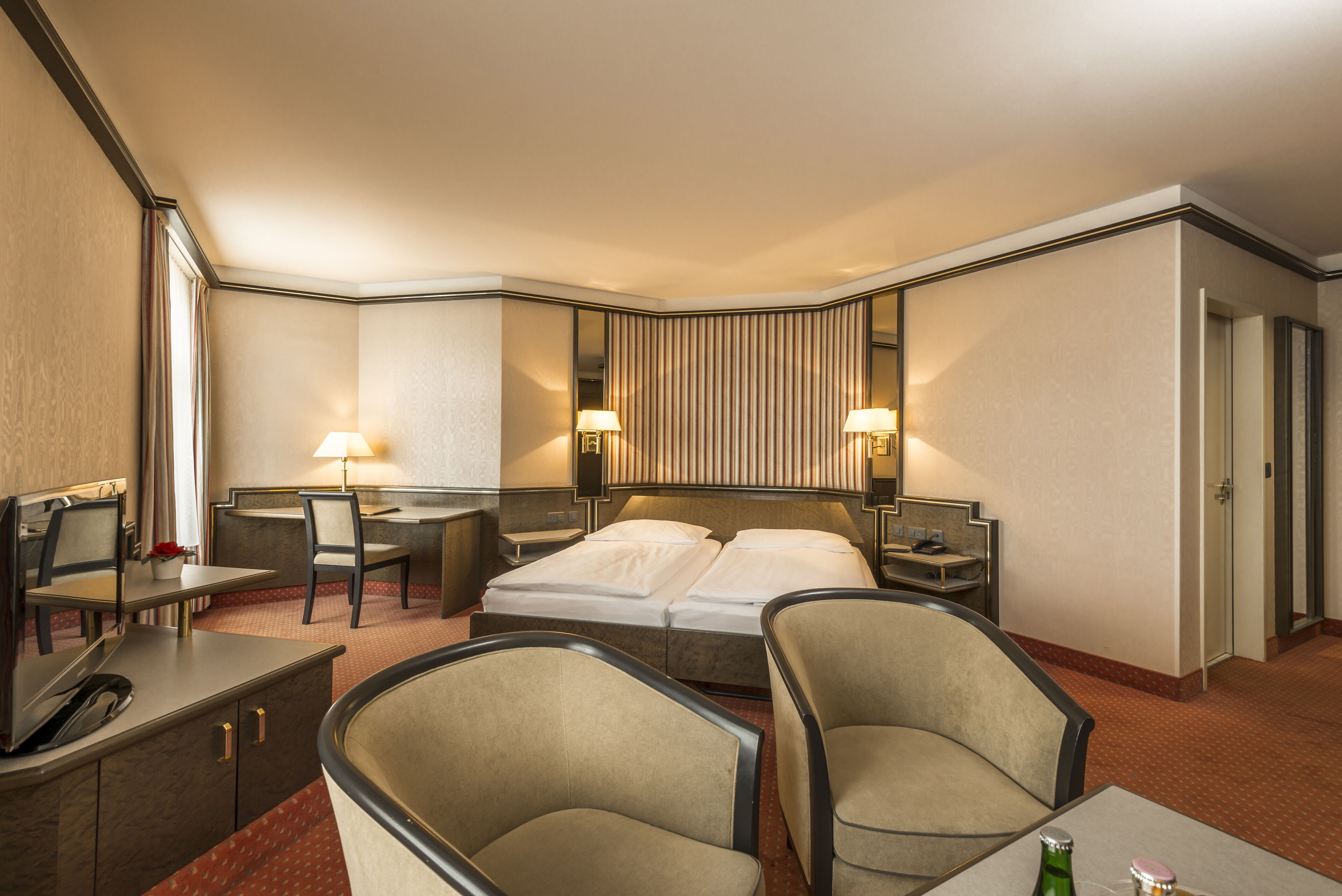Une chambre d’hôtel comprenant un lit, deux tables de chevet, un bureau, deux chaises et un miroir.