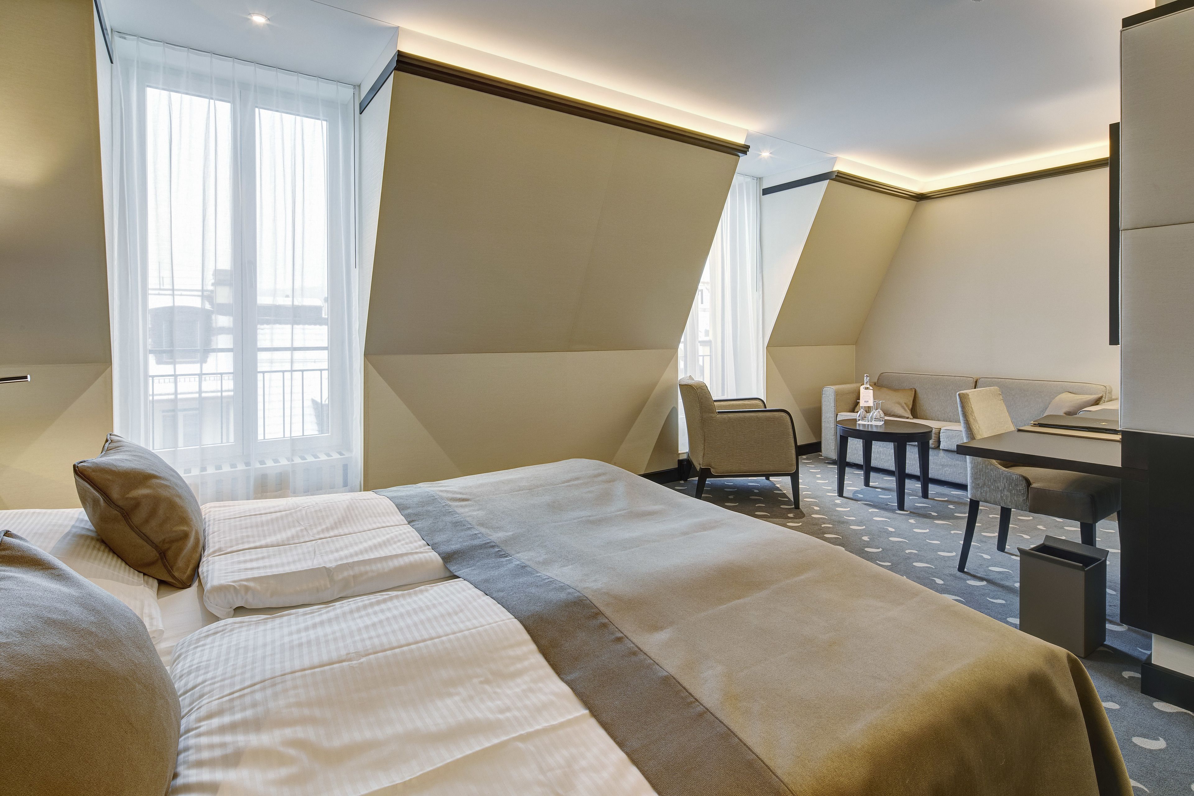 Une chambre d’hôtel avec un grand lit, un bureau et une chaise. Il y a une fenêtre avec des rideaux légers et une vue sur l’extérieur.