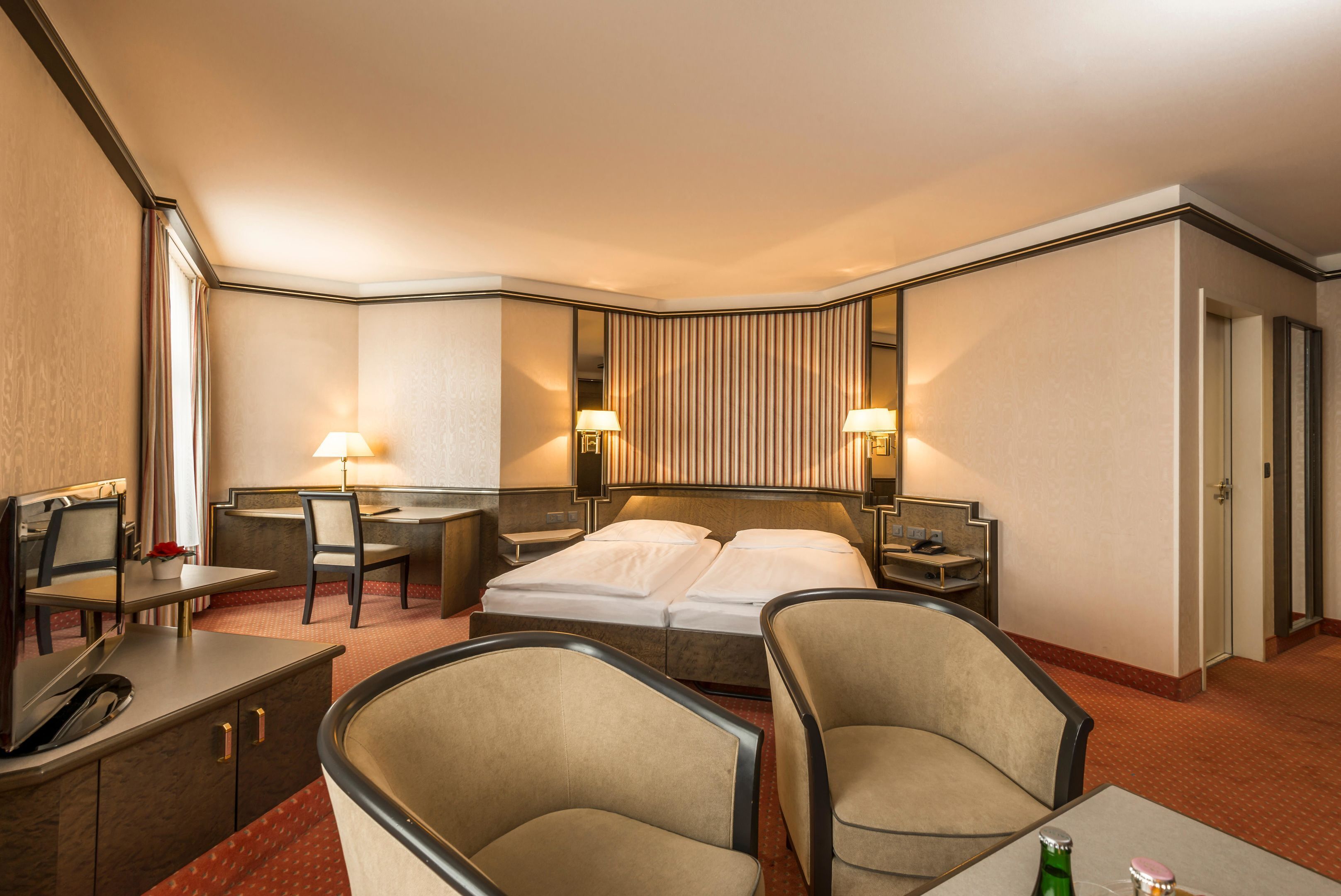 A hotel room with a bed, two bedside tables, a desk with a chair, a sofa, and a mirror.