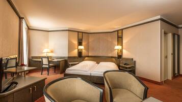 A hotel room with a bed, two bedside tables, a desk with a chair, a sofa, and a mirror.