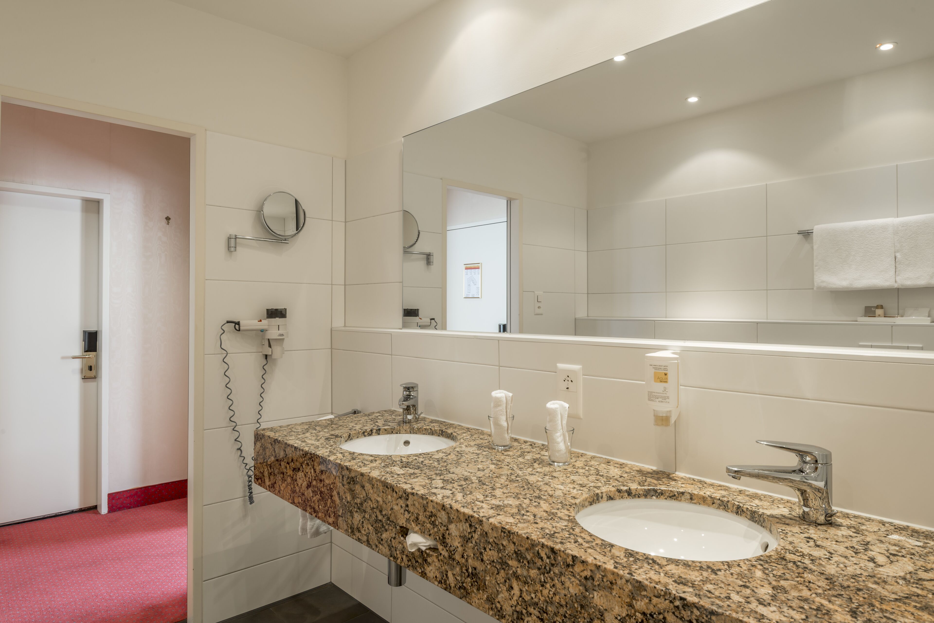 Een badkamer met twee wastafels, een grote spiegel en een vloer bekleed met rood tapijt.