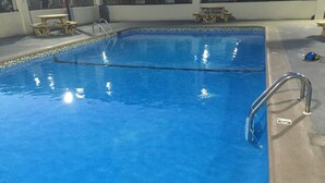 Una piscina rectangular con superficie de agua azul cristalina, una escalera metálica en un lateral y un borde alicatado.