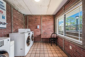 A laundry area with multiple washing machines, a table, and a chair.