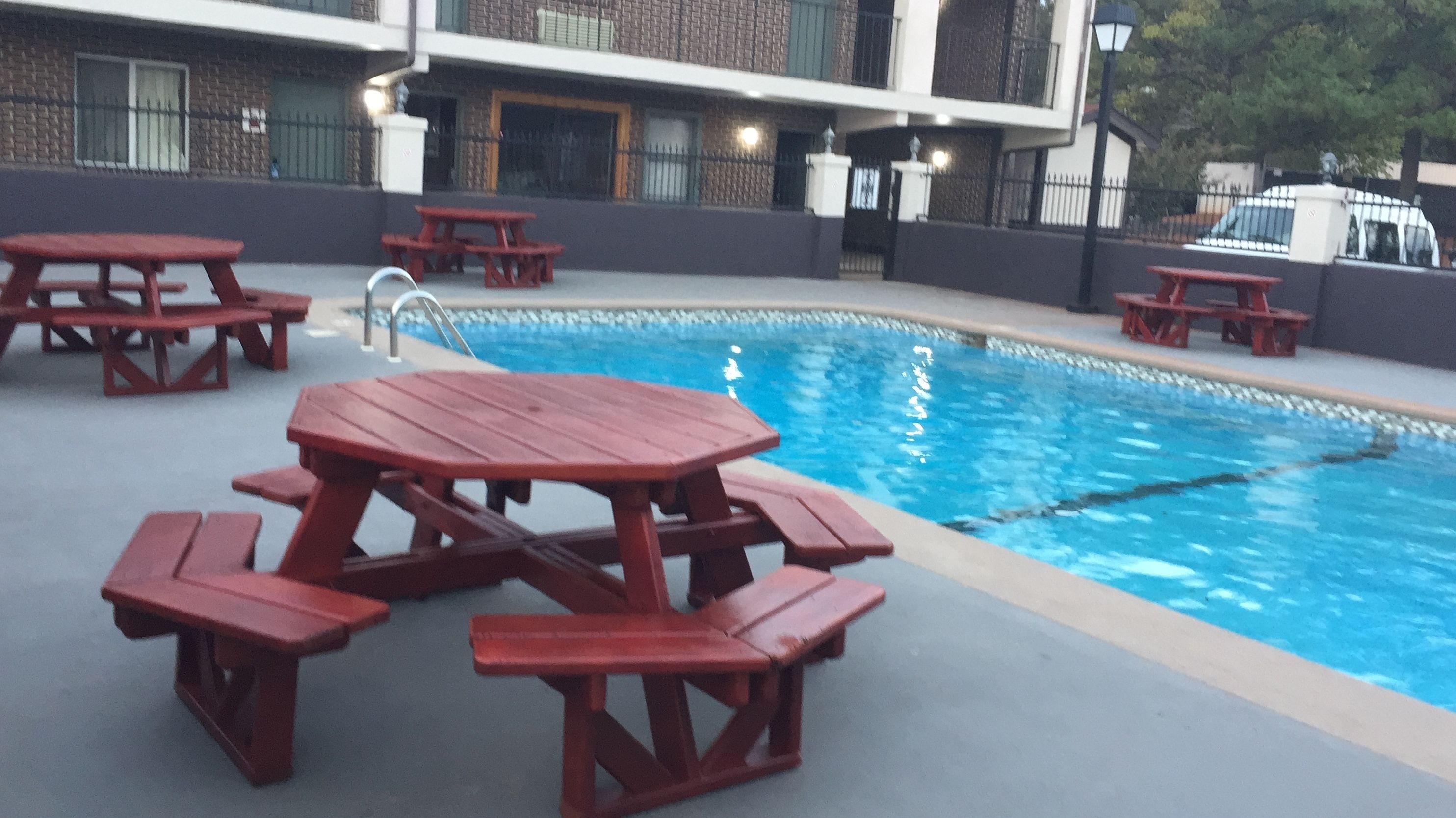 A swimming pool with red picnic tables and a building in the background.