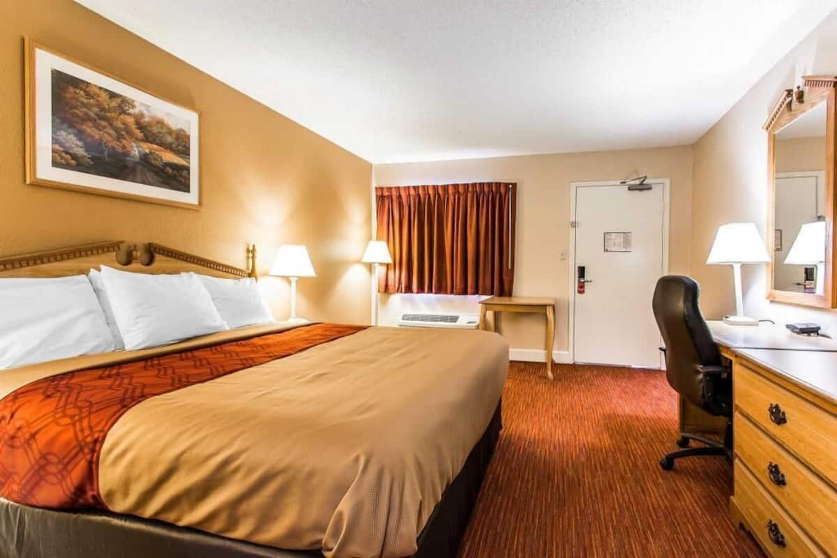 A hotel room with a bed, desk, chair, and a large mirror.