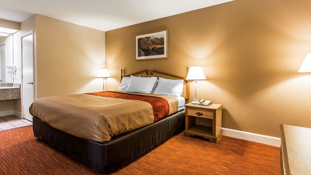 Una habitación de hotel con una cama grande, dos lámparas de noche, una mesita de noche y un cuadro en la pared.