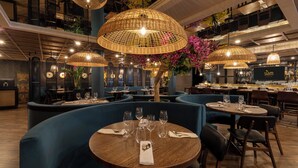 Un restaurante con mesas redondas, asientos tapizados en azul y lámparas colgantes de mimbre.
