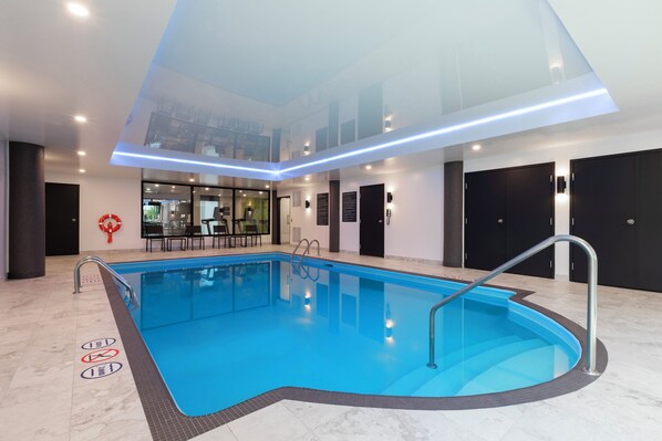 An indoor swimming pool with clear water, a glass ceiling, and modern lighting.