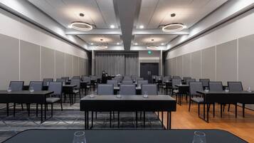 A conference room with rows of tables and chairs, a patterned carpet, and a modern ceiling design.