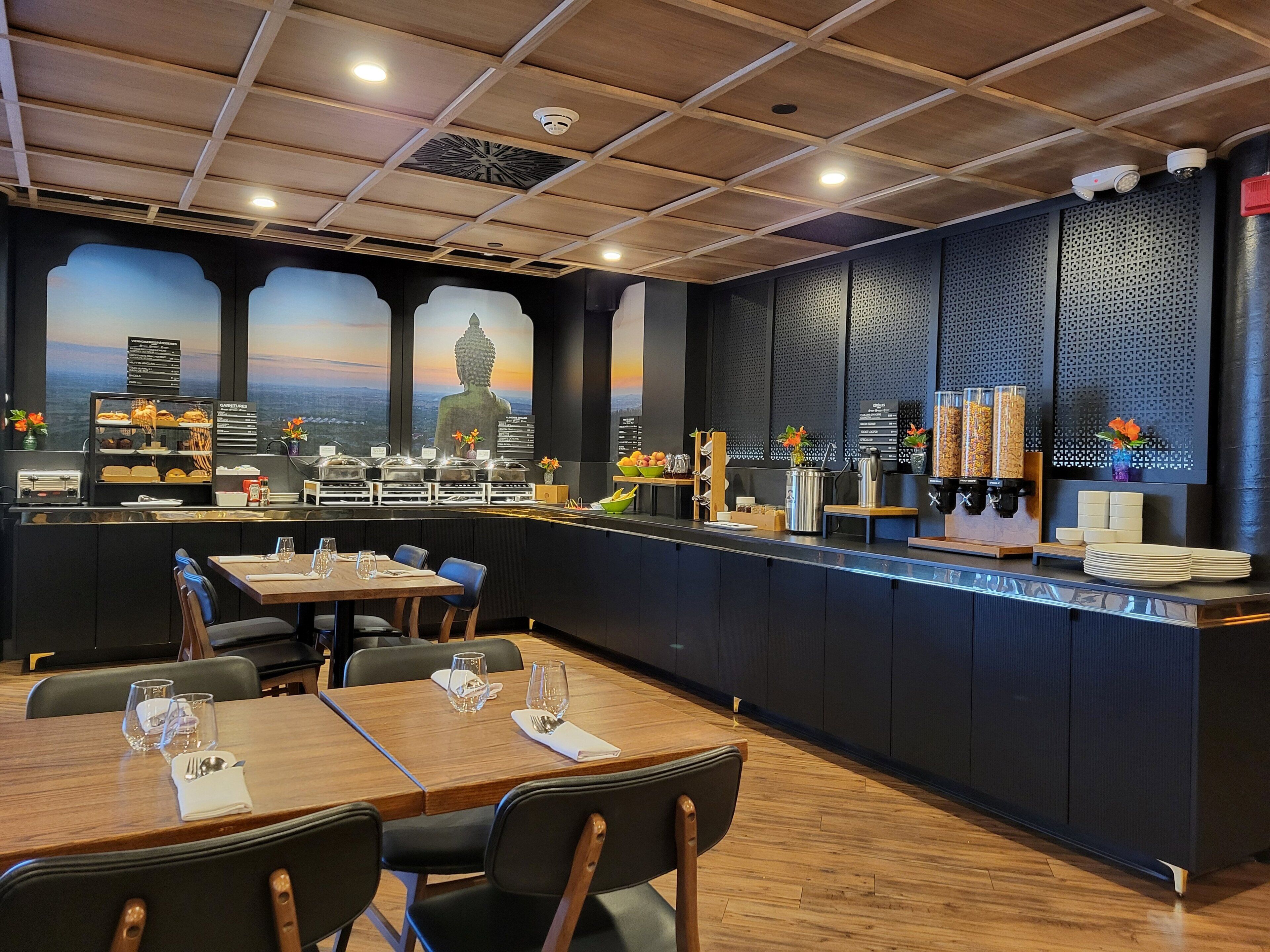 A restaurant with a counter, tables, chairs, and a Buddha statue mural.