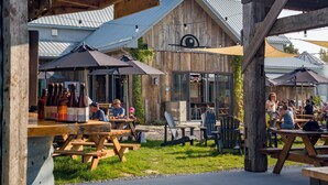 Un área de comedor al aire libre con mesas y sillas de madera, rodeada por un edificio rústico con techo de metal.