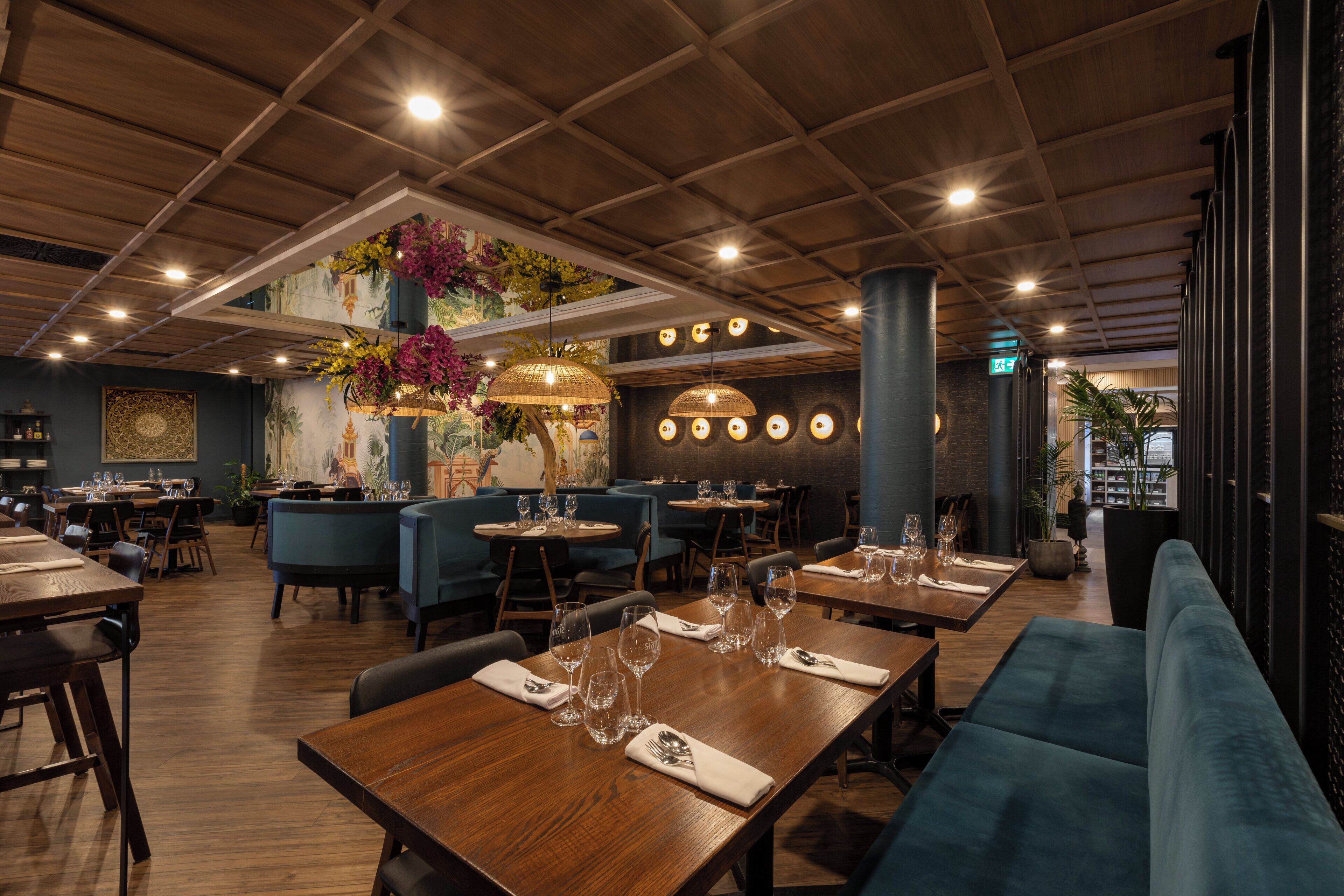 A restaurant with wooden tables, blue upholstered chairs, and hanging pendant lights.