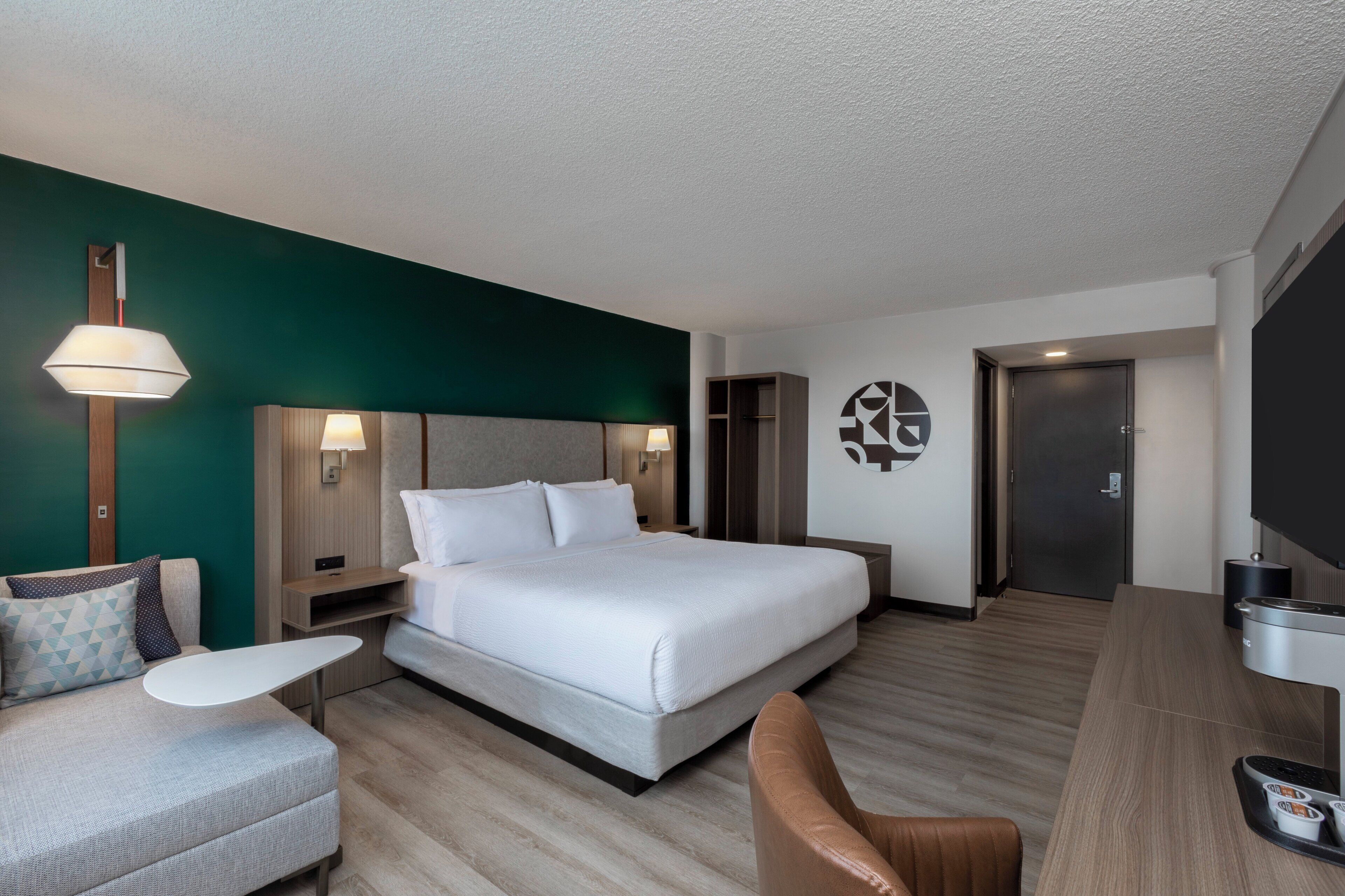 A modern hotel room with a large bed, a desk, a chair, and a TV.