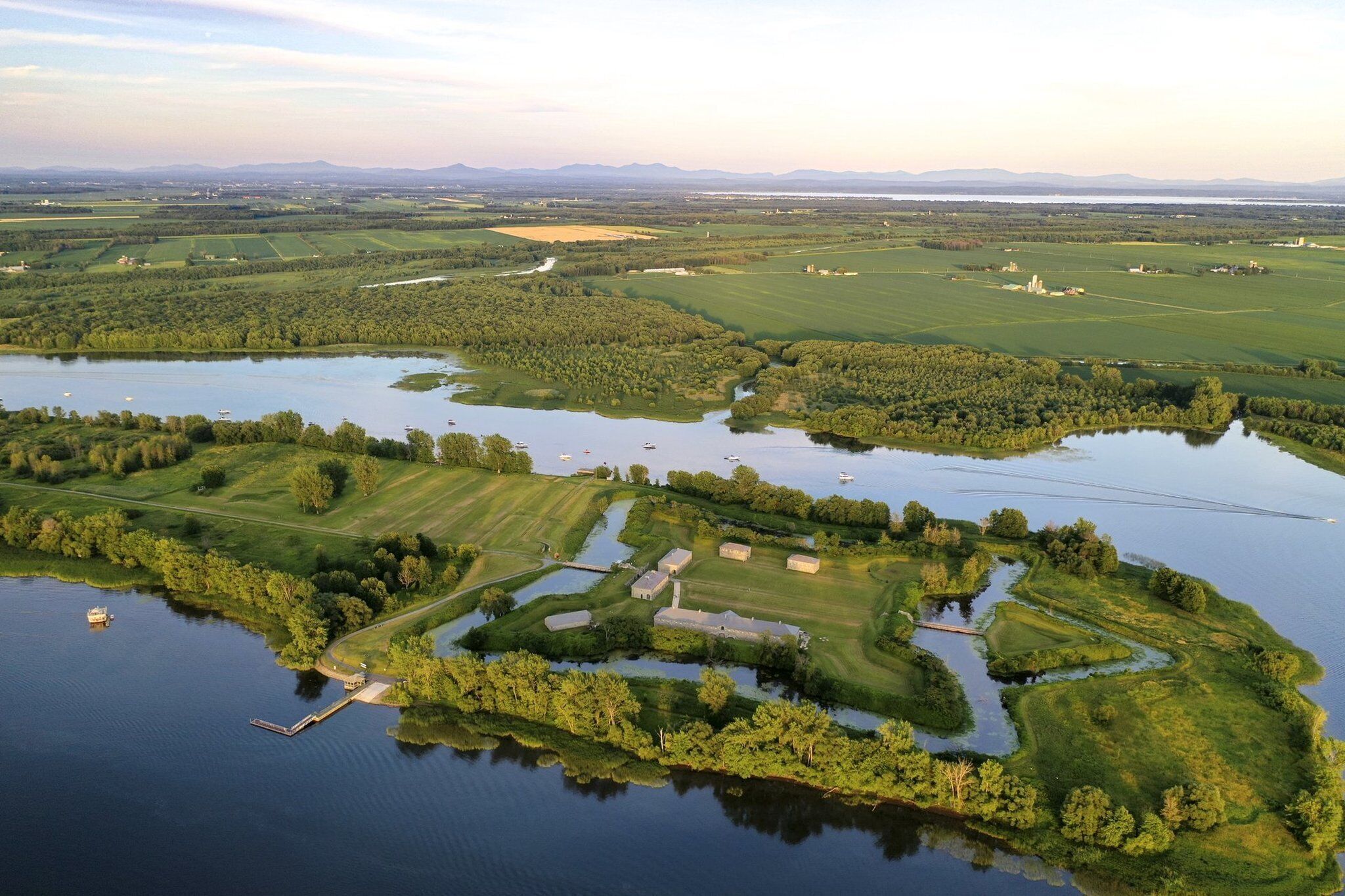 An aerial view of a large estate with multiple buildings, a lake, and surrounding fields.