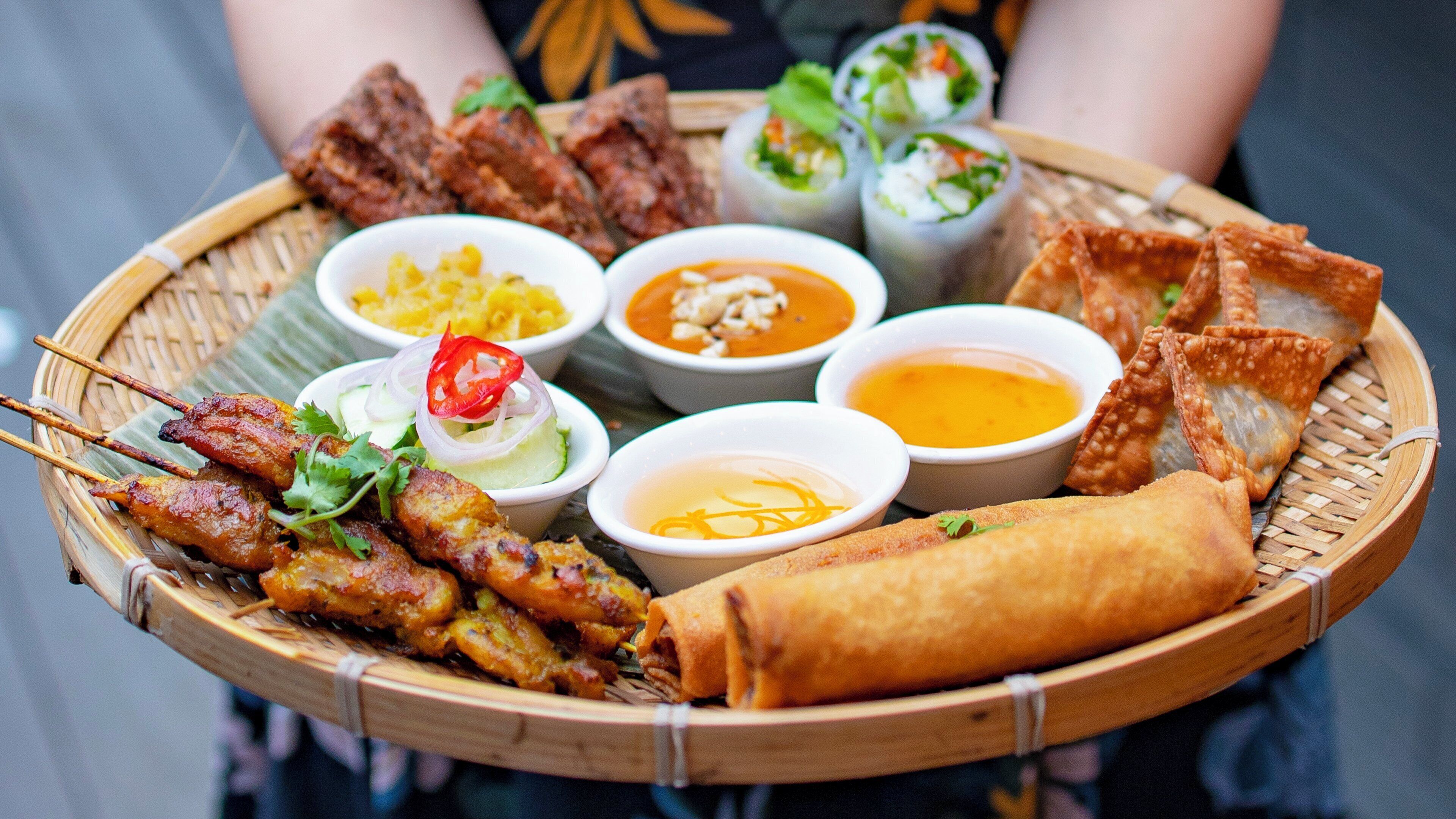 A tray of various dishes including skewers, spring rolls, and different sauces.