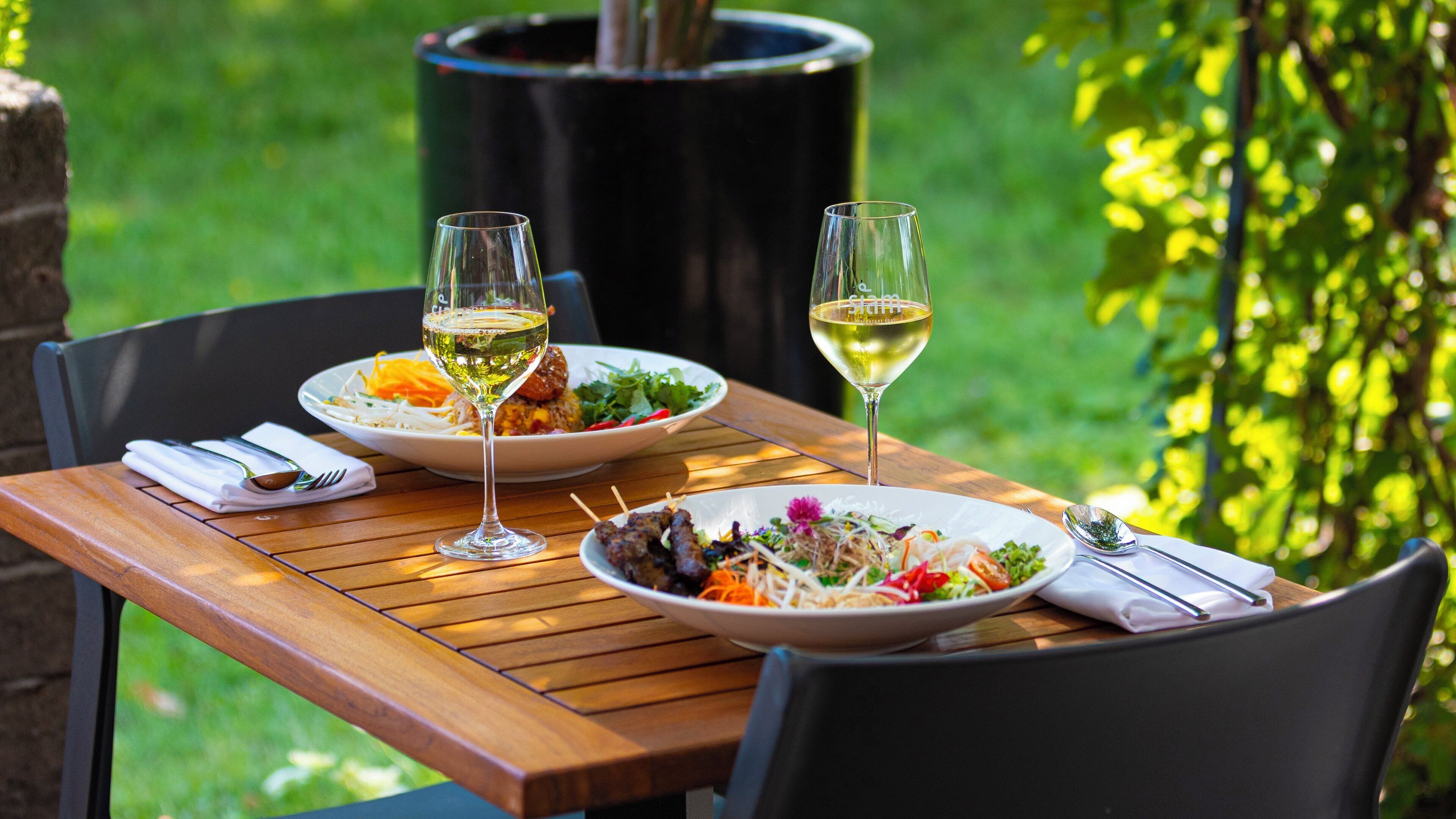 Une table en bois avec deux assiettes de nourriture et deux verres de vin blanc.