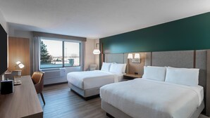 Habitación de hotel con dos camas, un escritorio y vistas a la ciudad.