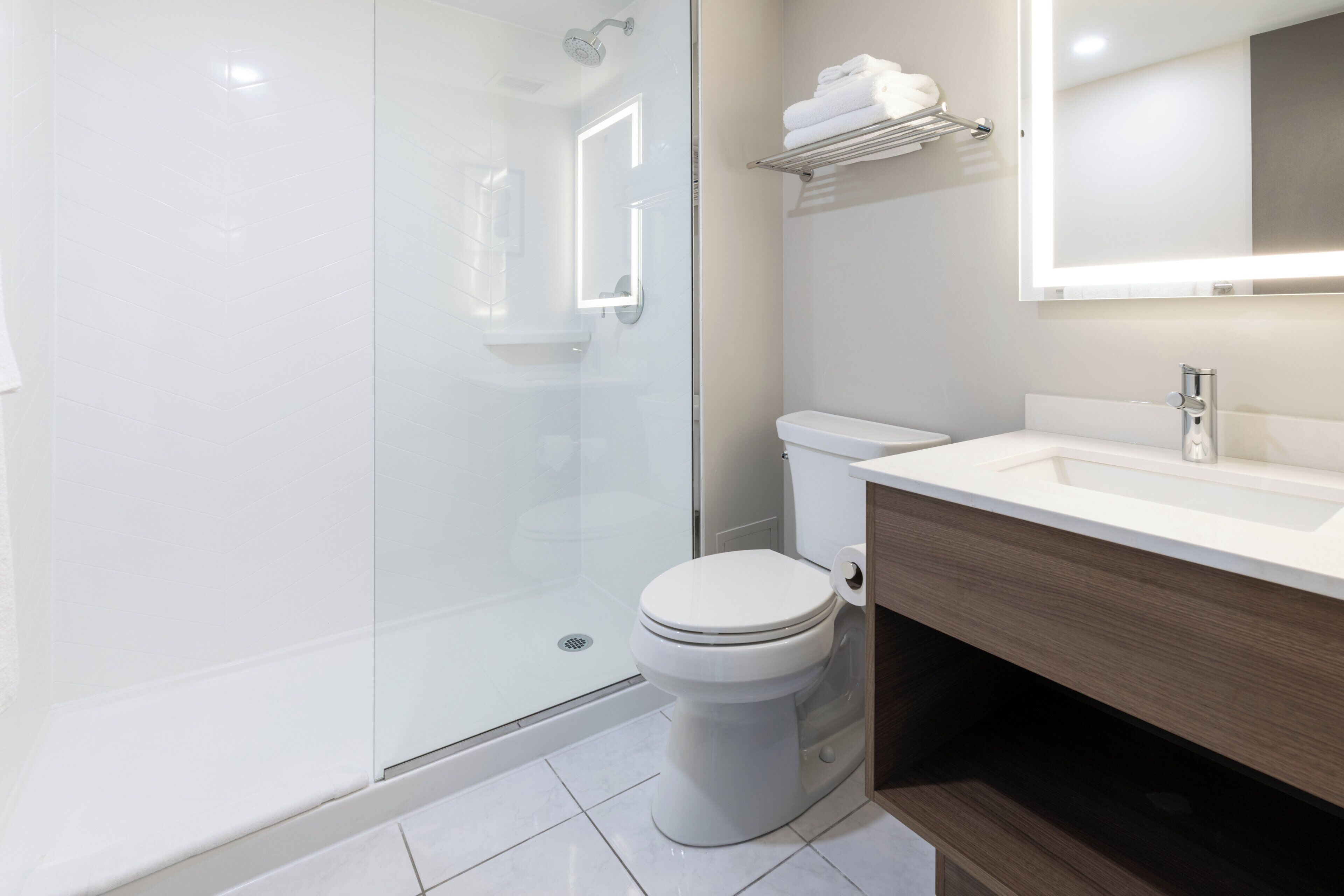 A modern bathroom with a glass shower enclosure, a white toilet, and a wooden vanity with a mirror.