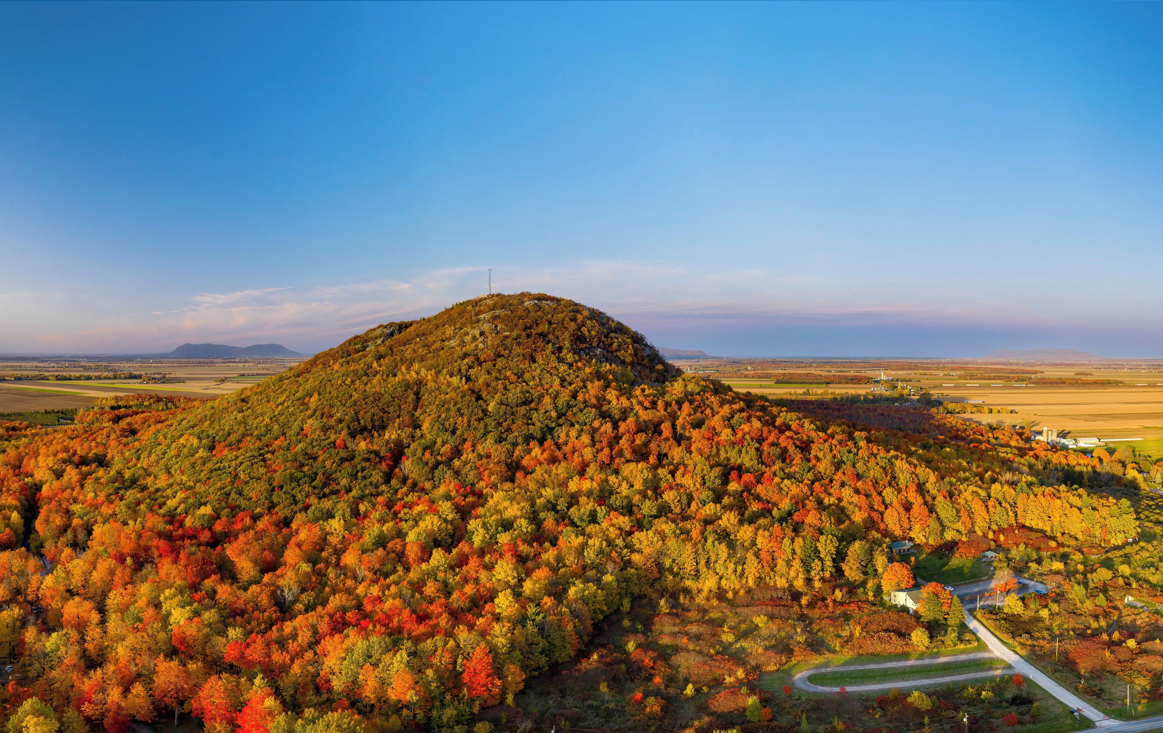 A hilltop with a road leading to a small building surrounded by autumn-colored trees.