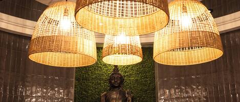 Un comedor con una estatua de Buda, lámparas colgantes de mimbre y una pared verde.