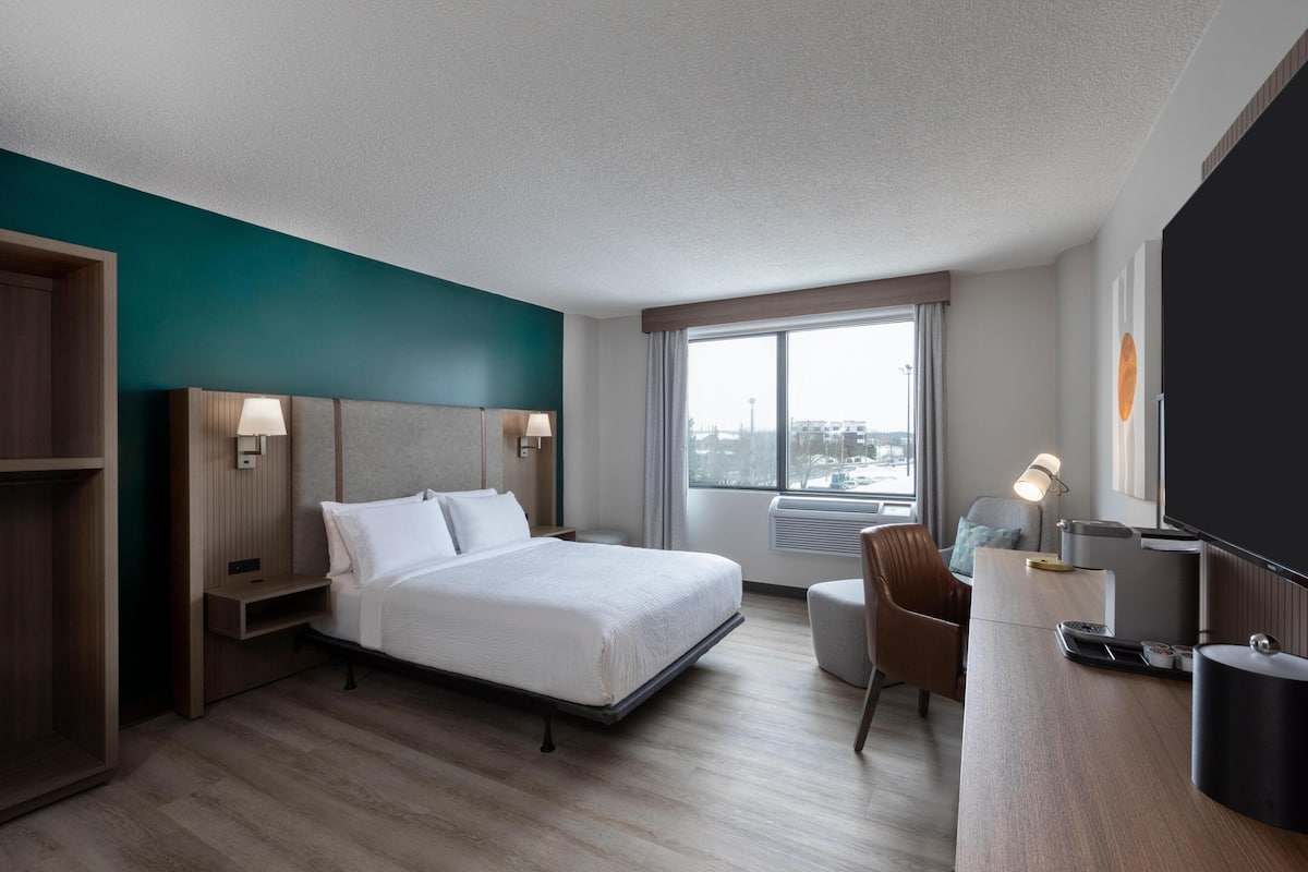 Une chambre d’hôtel avec un lit, un bureau, une chaise et une grande fenêtre.