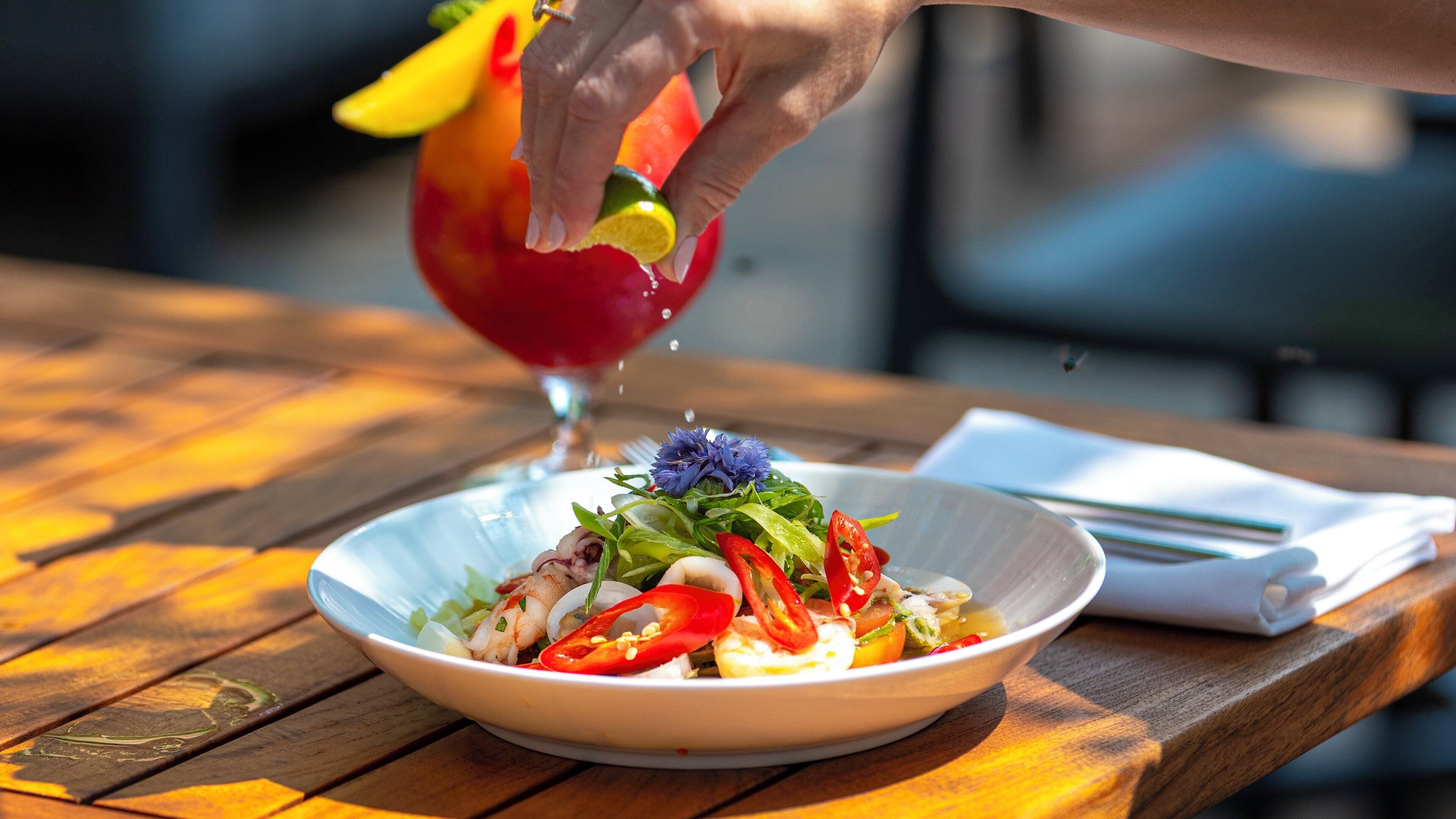 A bowl of salad with various vegetables and a decorative flower on a wooden table.
