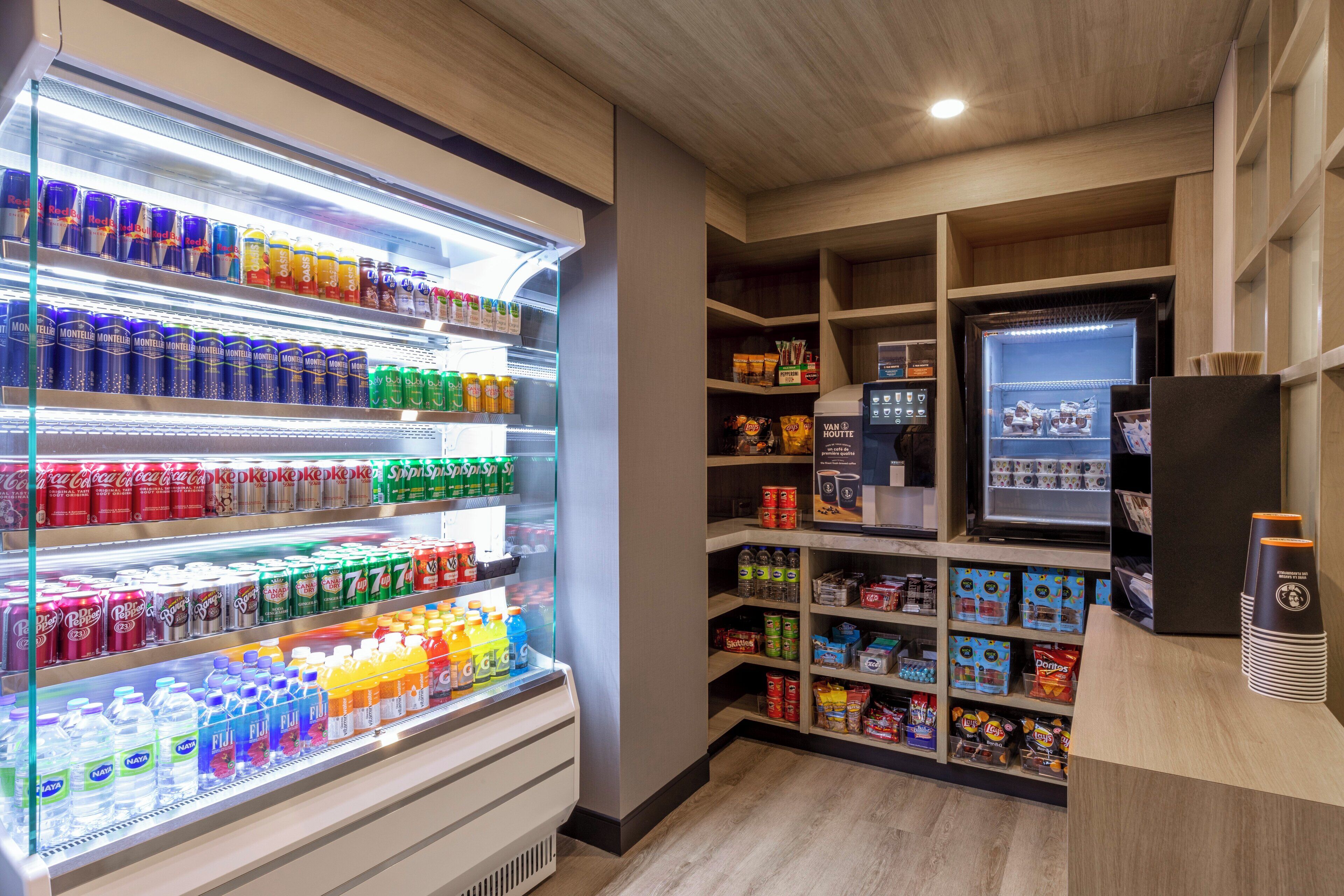 A well-lit beverage refrigerator stocked with various drinks, a vending machine, and shelves with snacks and other items.