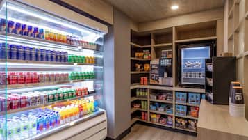 A well-lit beverage refrigerator stocked with various drinks, a vending machine, and shelves with snacks and other items.