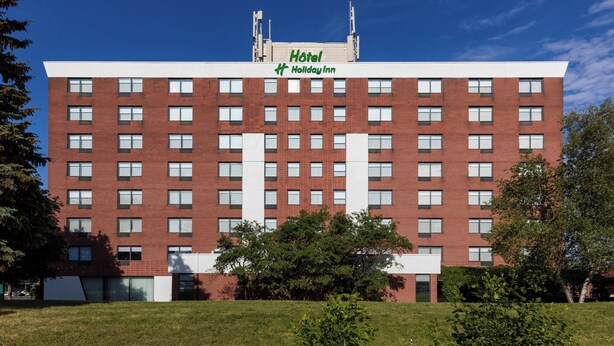 Un hotel de varios pisos con techo plano, un cartel que dice "Hotel Holiday Inn" y fachada de ladrillo.