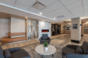 A modern lobby with seating areas, a reception desk, and a fireplace.