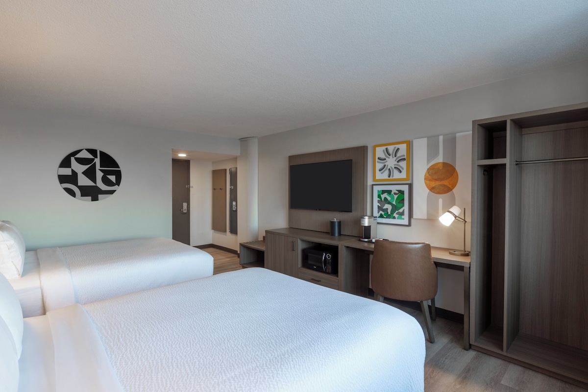 A hotel room with two beds, a desk, a TV, and a wardrobe.