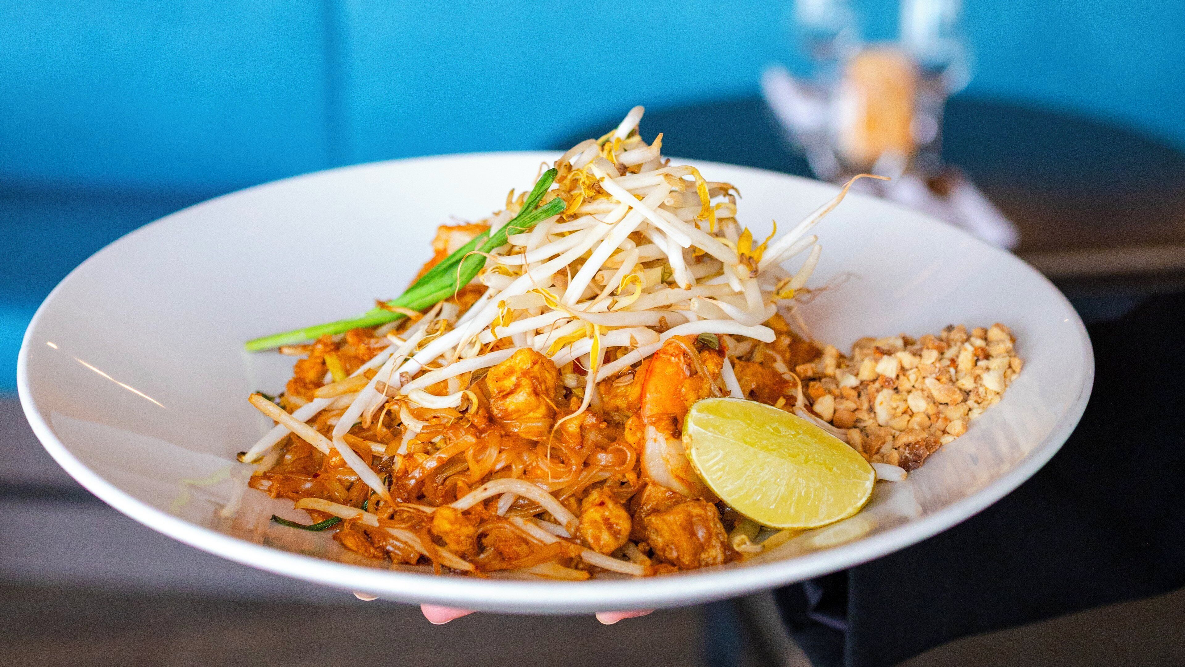 Een bord Pad Thai met tofo, limoen en gehakte pinda's.