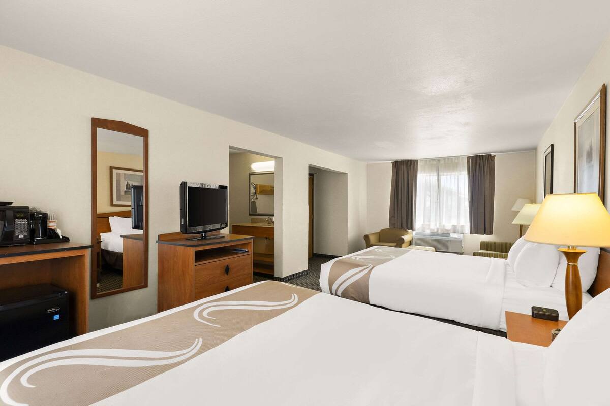 Ein Hotelzimmer mit zwei Betten, einem Schreibtisch, einem Fernseher, einer Kaffeemaschine und einer Lampe.