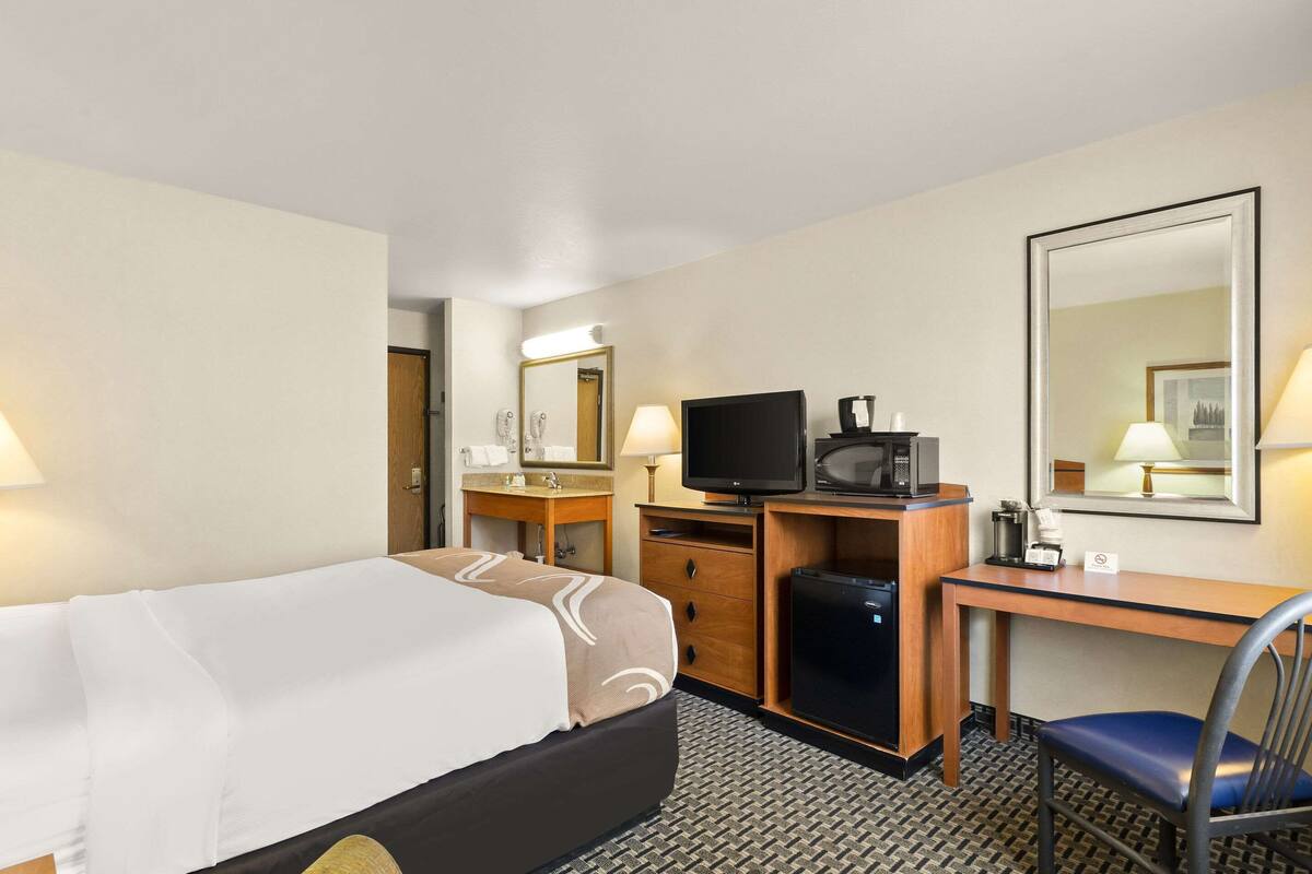 Ein Hotelzimmer mit Bett, Schreibtisch mit Computer, Fernseher und Spiegel.