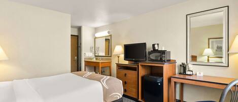 A hotel room with a bed, a desk with a computer, a television, and a mirror.