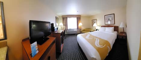 Habitación de hotel con cama, televisor, escritorio, silla y ventana con cortinas.