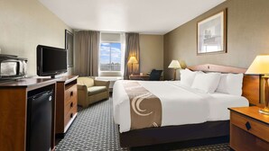 A hotel room with a bed, a desk with a television, a chair, a desk lamp, and a window with curtains. - Quality Inn Cheyenne I-25 South (Cheyenne)