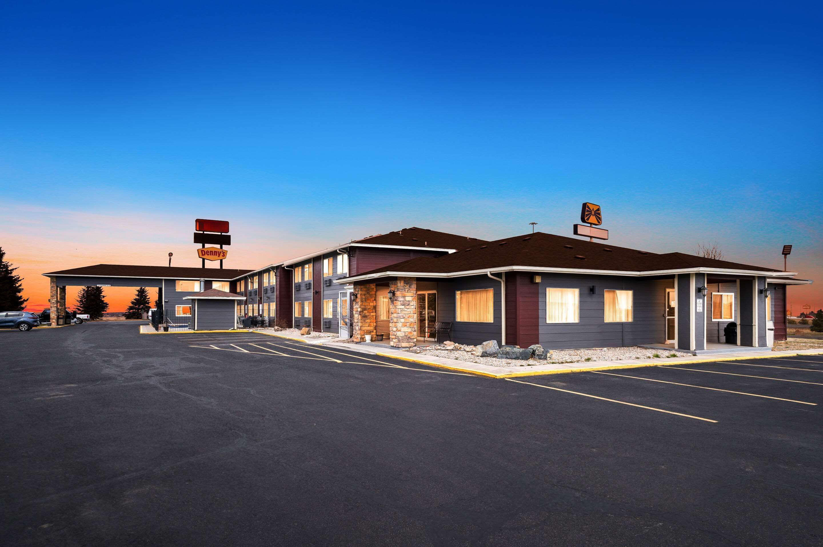 A motel with a parking lot, a gas station, and a sign for 'Denny's' in the background.